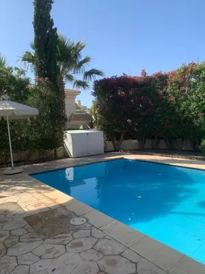a large blue swimming pool with an umbrella and trees at Villa 28 Protaras in Protaras