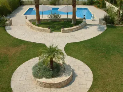 a walkway around a pool with a palm tree at Three bedroom villa with private pool and landscaped garden close to the beach in Pissouri