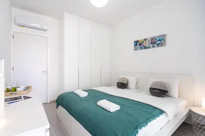 a white bedroom with a bed with a green blanket at Lana 1-Bedroom Apt in Larnaca in Larnaka