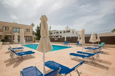 a pool with blue chairs and white umbrellas at Ayia Napa Holiday Apartment Na101 in Ayia Napa