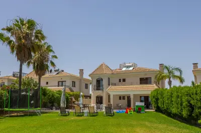 a large house with a yard with chairs and palm trees at SunnyVillas: 4BR SeaFront Villa*Private Pool*BW44 in Protaras