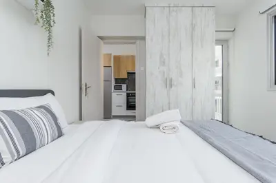 a white bedroom with a white bed and a kitchen at Amore 2-BR Apt By Finikoudes in Larnaka