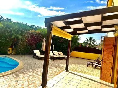 a patio with chairs and an umbrella and a pool at Villa Victoria Ayia Napa in Ayia Napa