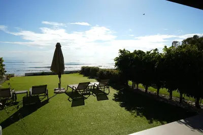 a lawn with chairs and an umbrella and the ocean at Meneou Houses by the Sea in Larnaka