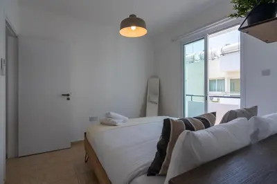 a white bedroom with a bed and a window at Chloris 3- Bedroom Apartment W/Pool in Larnaca in Larnaka