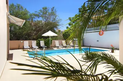 a swimming pool with chairs and an umbrella at Villa Michaella - 500m from Golden Beach in Paralimni