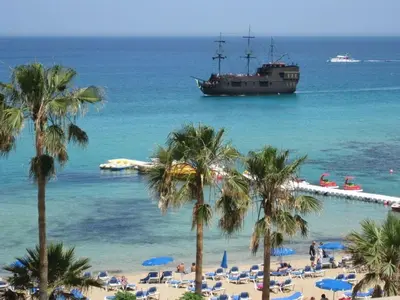 a boat in the water next to a beach with palm trees at My Mythical Pearl in Protaras