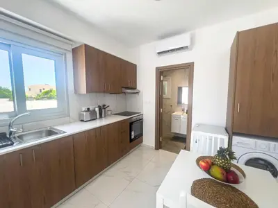 a kitchen with wooden cabinets and a table with a bowl of fruit at Musan Boutique Apartments in Ayia Napa