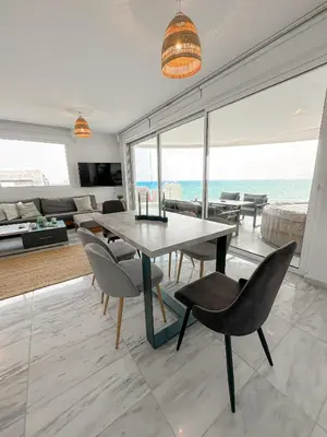 a living room with a table and chairs and the ocean at Seaview Pearl in Mackenzie with Pool & Jacuzzi in Larnaka