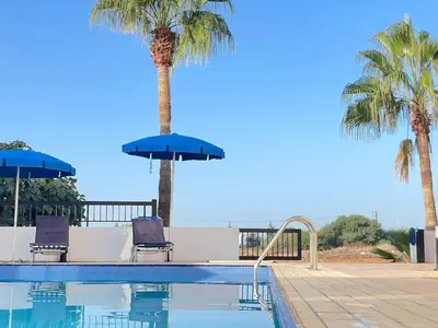a swimming pool with two palm trees and two blue chairs at Sunset Pearl Holiday Villa in Ayia Napa