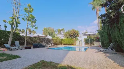 a swimming pool with chairs and umbrellas in a yard at Nissi 86 Apartment - Luxcyservices in Ayia Napa