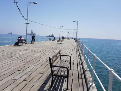 a wooden pier with people sitting on benches on the water at Chariandry Residence, Limassol City Centre in Limassol