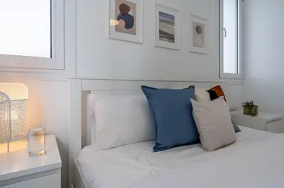 a white bedroom with a bed with blue and white pillows at Artemis 1-Bedroom Apartment in Larnaca in Larnaka