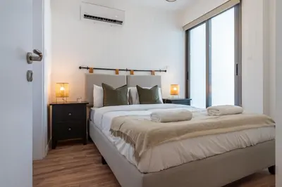 a white bedroom with a large bed and a window at Latte's Prime 1-Bedroom Apartment in Larnaca in Larnaka