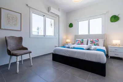 a bedroom with a bed and a chair and two windows at Diamond’s 2-Bedroom Apartment in Larnaca in Larnaka