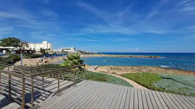 a boardwalk leading to a beach with people in the water at Dream Beach House Steps from the Sea & Free Parking in Protaras
