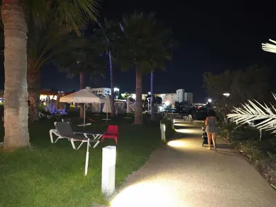 a woman walking down a path at night with palm trees at Dream Beach House Steps from the Sea & Free Parking in Protaras
