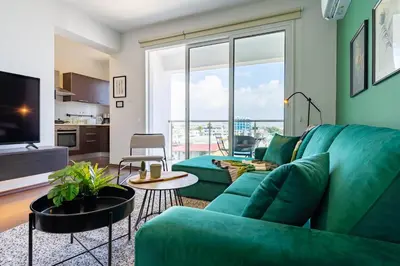 a living room with a green couch and a large window at Harbor Apartments in Larnaca in Larnaka