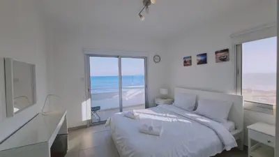 a white bedroom with a bed and a view of the ocean at STAY Beach Wave Apartment in Larnaka