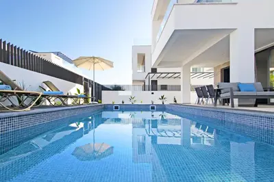 a swimming pool with chairs and an umbrella next to a building at Villa Daniella in Protaras