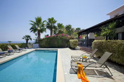 a swimming pool with chairs and a table next to a house at Ayios Elias Pearl in Protaras