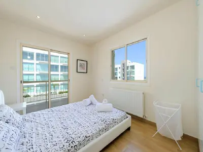a white bedroom with a bed and two windows at Theodora in Protaras