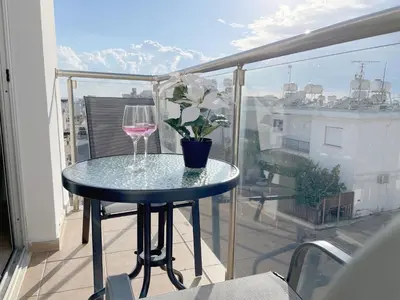 a table with a wine glass and a potted plant on a balcony at Sunset Pearl Holiday Apt. - Ayia Napa in Ayia Napa