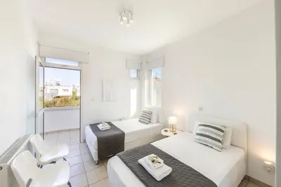 a white room with two beds and a chair at Faros Seaside Villa Larnaca in Pervolia