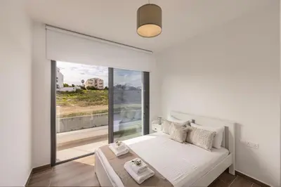 a white bedroom with a bed and a large window at Protaras By the Bay Villa 33 in Protaras