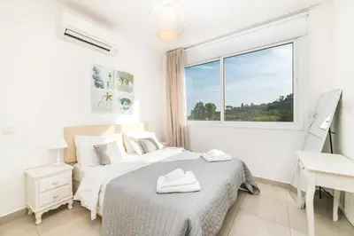a white bedroom with a bed and a desk and a window at Green Bay Villa #17 in Protaras