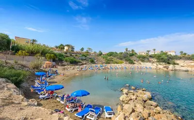 a beach with chairs and umbrellas and people in the water at Villa Clementine in Protaras