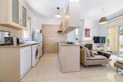 a kitchen with white appliances and a living room at Villa Clementine in Protaras