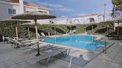 a swimming pool with chairs and umbrellas next to a building at STAY White Petals Apartment in Larnaka