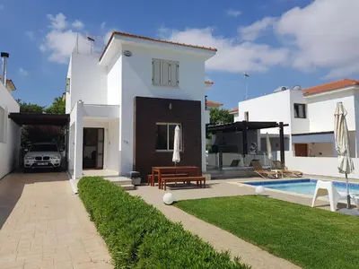 a white house with a swimming pool and a yard at POSEIDONIA BEACH GARDENS in Paralimni