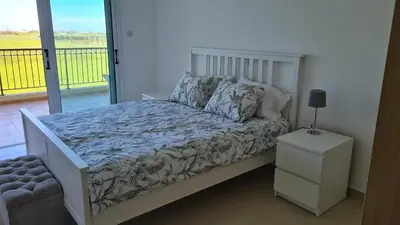 a bed in a bedroom with a view of a balcony at The Olive Grove Escape, Eleonas Apts in Sotira