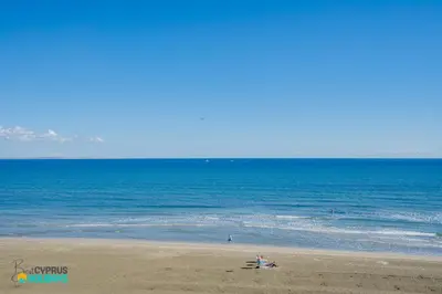 a beach with people sitting on the sand and the ocean at Makenzy Sandy Beachfront Paradise in Larnaka