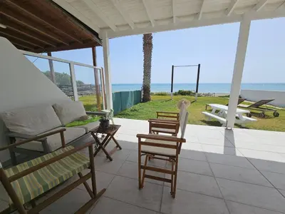 a porch with a bed and chairs and the ocean at Ammos Beachfront Villa Paradise in Larnaka
