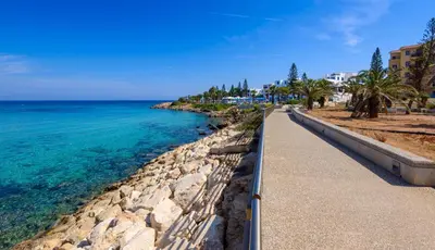 a walkway next to the ocean with palm trees at Villa Marilena in Protaras