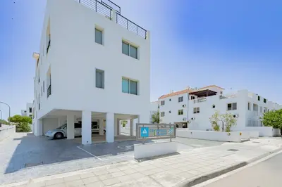 a white building with a car parked in a parking lot at Stylish One-Bedroom Sea Retreat in Paralimni