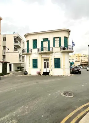 a white building with green shuttered windows on a street at Le Voyageur II in Larnaka