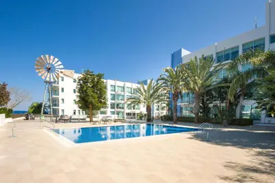 a swimming pool in front of a building with a windmill at Alessia 2bed Apartment - Coralli Beachfront Resort in Protaras