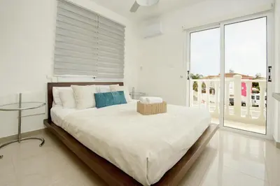 a white bedroom with a large bed and a large window at Villa Thetida in Ayia Napa