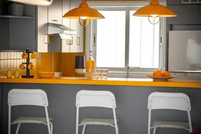 a kitchen with three stools at a counter with orange lights at Protaras O2 Seaside Suite in Protaras