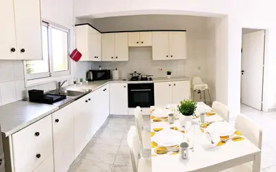 a kitchen with white cabinets and a white table and chairs at Large apartment close to Finikoudes Beach with 2 balconies in Larnaka