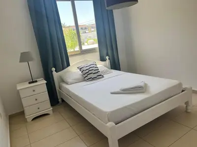 a bedroom with a bed and a window with blue curtains at Eliza Suite at Pernera Beach in Protaras