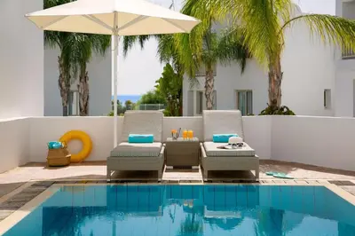 a patio with two chairs and an umbrella next to a pool at Dazzling Protaras Villa Villa Akame 3 Bedrooms Beachfront in Protaras