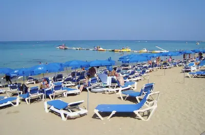 a beach with many chairs and blue umbrellas at Dazzling Protaras Villa Villa Akame 3 Bedrooms Beachfront in Protaras