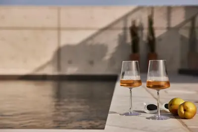 two wine glasses sitting on a table next to a pool at White City Limassol in Limassol