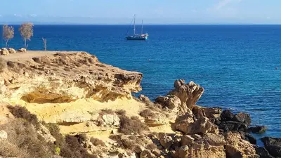 a boat in the ocean next to a rocky shore at Mythical Sands resort - Hana in Paralimni