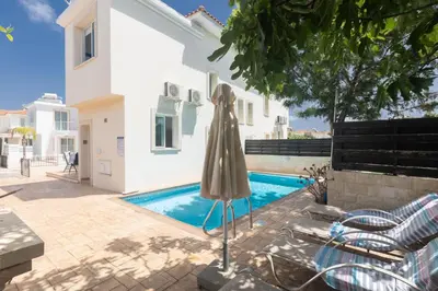 a pool with an umbrella next to a house at Protaras Orestiada Villa OV14 in Protaras